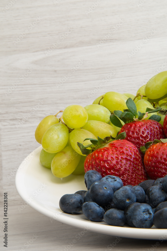 Fresh fruits on a wooden background. Strawberries, grapes, blueberry closeup