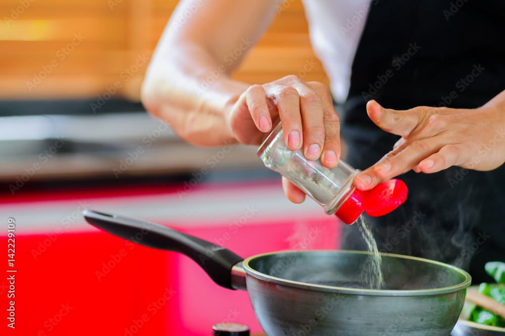 Private Thai chef cooking in a modern style home kitchen. Making Thai food, adding paper, face hidden. Close up hands