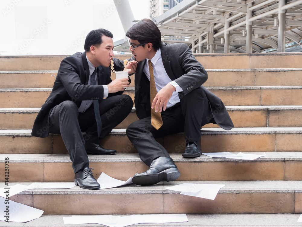 Two office workers sitting and eating noodles outdoor tired after job interview