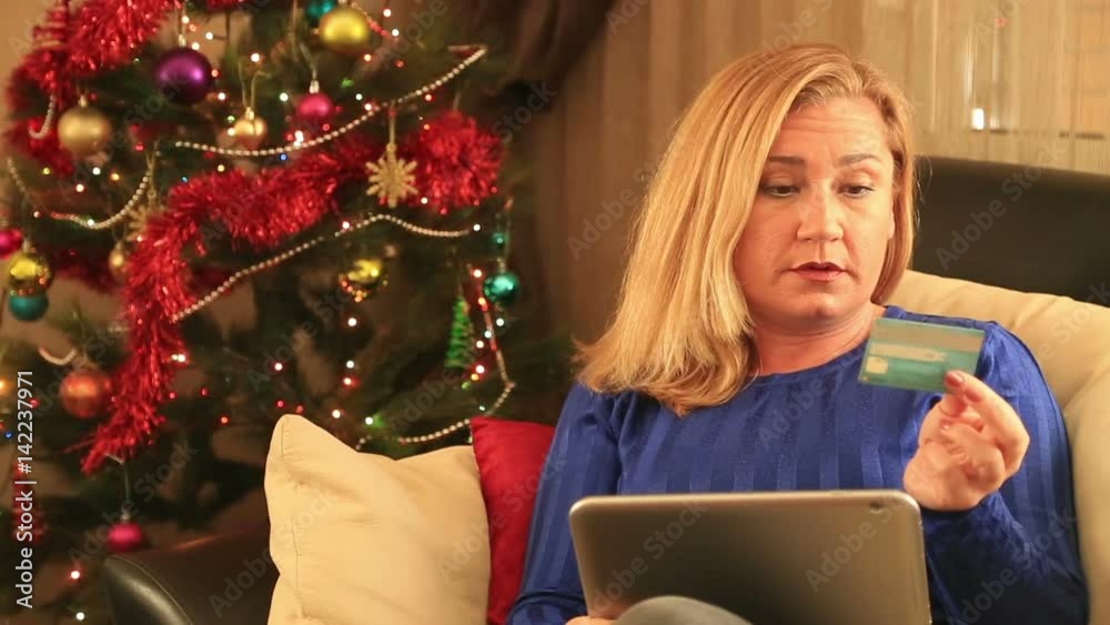 Happy online shopping woman with digital tablet computer sitting on a sofa in front of a christmas tree. Christmas, x-mas, winter, happiness concept Happy online shopping woman with digital tablet computer sitting on a sofa in front of a christmas tree. Christmas, x-mas, winter, happiness concept