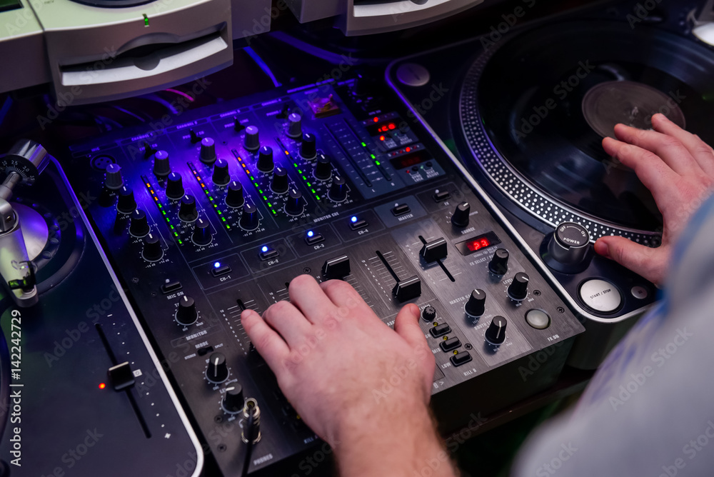 Close up Dj hands on equipment deck and mixer with vinyl record at party. Top view, selective focus