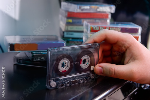 Close up man's hand with CD audio cassette standing on the old fashiones cd playern with backgroud of stack of audio cassettes. Selective focus photo