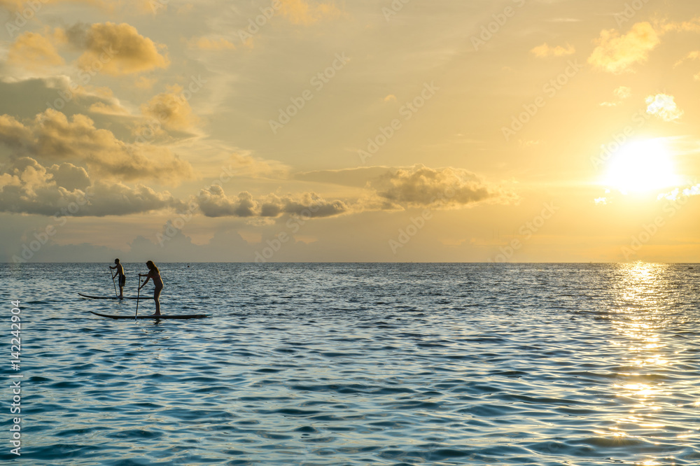 Couple stand up paddle boarding on quiet sea at sunset