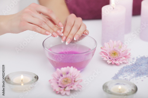 Spa Beauty Salon. Closeup Of Female Hands With Perfect Natural Fingernails Soaking In Hand Bath Before Manicure. Woman Washing Perfect Nails In Transparent Bowl Of Water. Nail Care. High Resolution