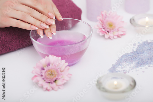 Spa Procedure. Woman In Beauty Salon Holding Fingers In Aroma Bath For Hands. Closeup Of Female Nails Soaking In Bowl Of Water With Pink Flower Petals. Aromatherapy. High Resolution