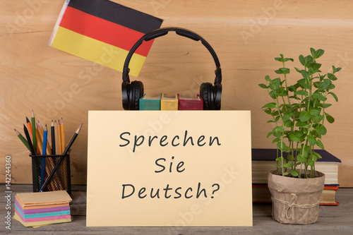 Fototapeta papier z tekstem „sprechen sie deutsch?”, flaga Niemiec, książki, słuchawki, ołówki