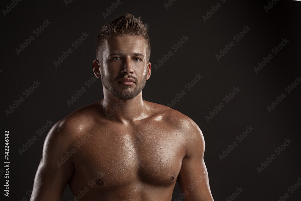 Model man with an open  chested on a dark background , muscular body of a young man in jeans . Shot in a studio .