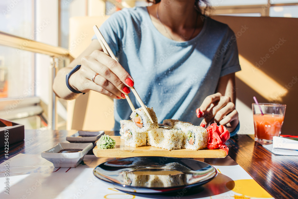 Woman in the blue shirt is eating at a sushi restaurant in summer Woman in the blue shirt is eating at a sushi restaurant in summer