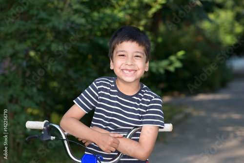 the boy with bicycle stands on the street and smiles