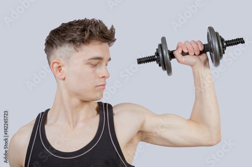 Strong teenage boy exercising by lifting weights