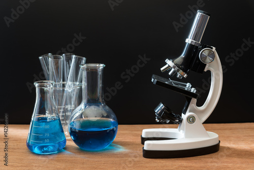 science laboratory test tubes and white microscope on wooden table with black background , laboratory equipment