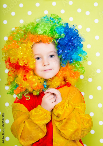 A cheerful clown in an iridescent wig and huge boots stands on a luscious bright green background in polka dots