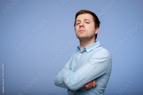 Fototapeta A young handsome man in a blue shirt looks confidently at the camera