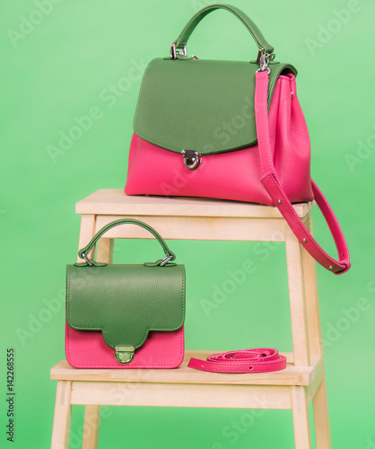 Fashion styled woman's handbags in pink and green colors standing on a wooden chair on green background photo