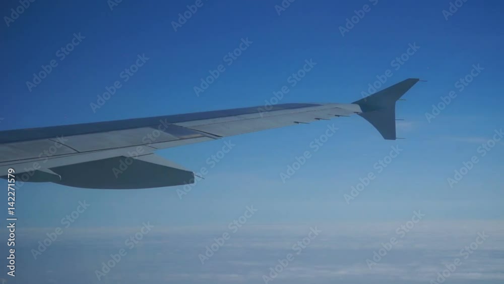 A view of the wing of an airplane through a window against a background of a blue evening sky with clouds. A view of the wing of an airplane through a window against a background of a blue evening sky with clouds.