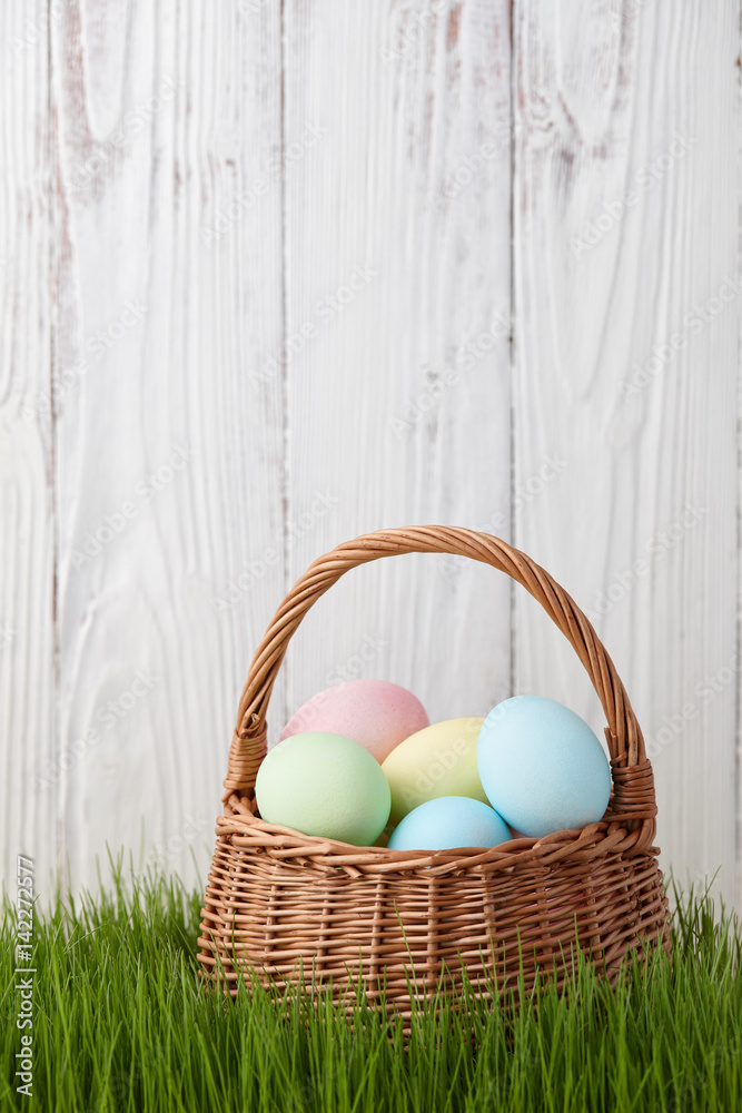 Colorful easter eggs basket in a grass meadow on white fence background Colorful easter eggs basket in a grass meadow on white fence background