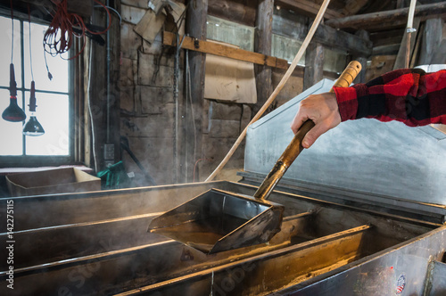 steam rising off of boiler evaporating  maple tree sap to make maple syrup in sugar house, worker ladling syrup to test  how thick syrup has become ; an early spring tradition in Vermont 
