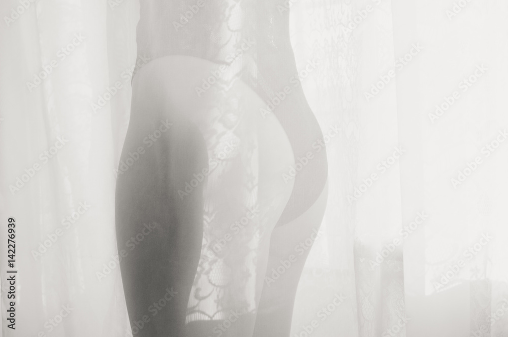 Obraz premium Woman silhouette behind transparent curtain on light window sunny background abstract