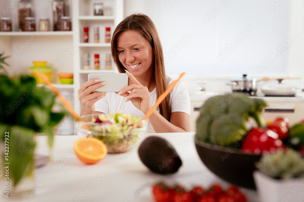 Beautiful young woman taking photo of healthy salad with smartphone for her blog.