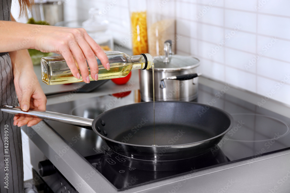 Closeup of woman pouring oil on frying pan Closeup of woman pouring oil on frying pan