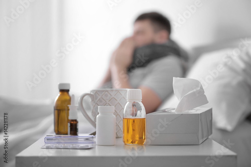 Medicines and cup of hot tea with blurred ill man on background