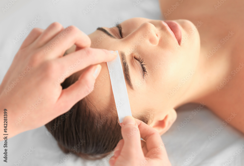 Beautician waxing young woman's eyebrows in spa center Beautician waxing young woman's eyebrows in spa center