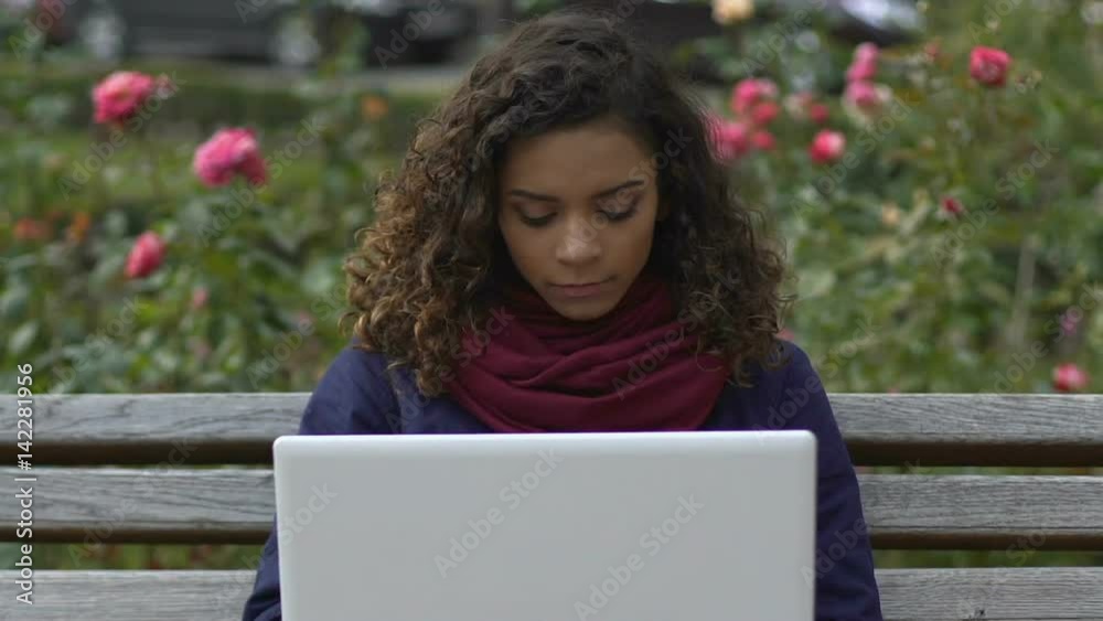 Pretty mixed race lady opening laptop and chatting with boyfriend at park