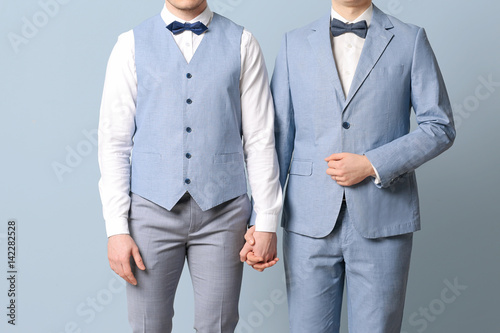 Happy gay couple holding hands together on color background photo