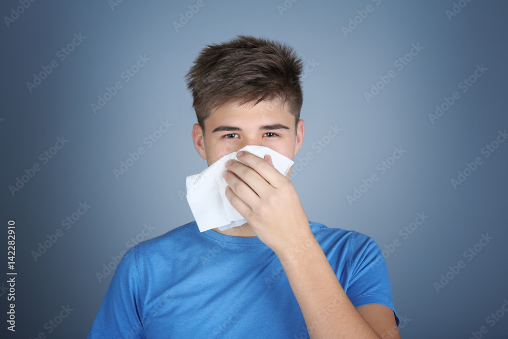 Young man blowing nose on tissue against color background Young man blowing nose on tissue against color background