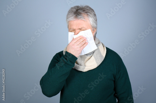 Senior man blowing nose on ...