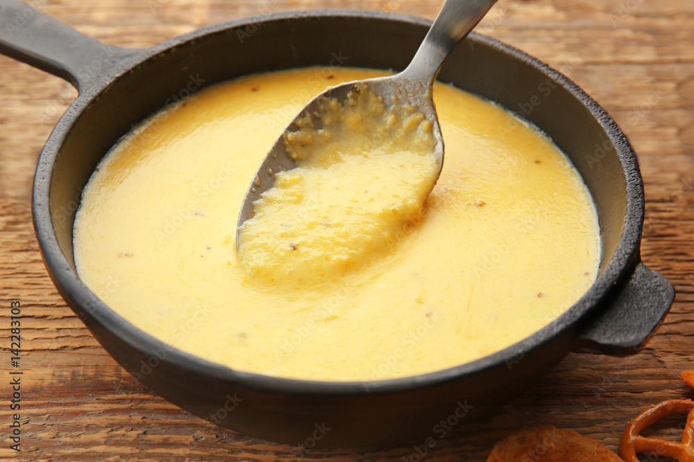 Frying pan of creamy cheese with spoon on wooden background Frying pan of creamy cheese with spoon on wooden background