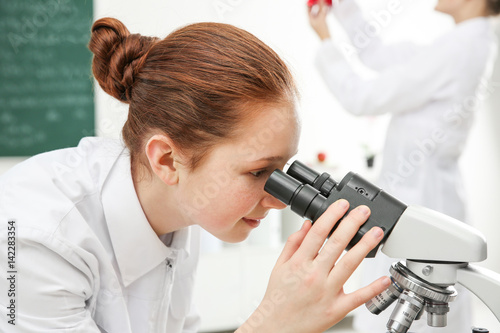 Beautiful school girl looking through microscope in chemistry class