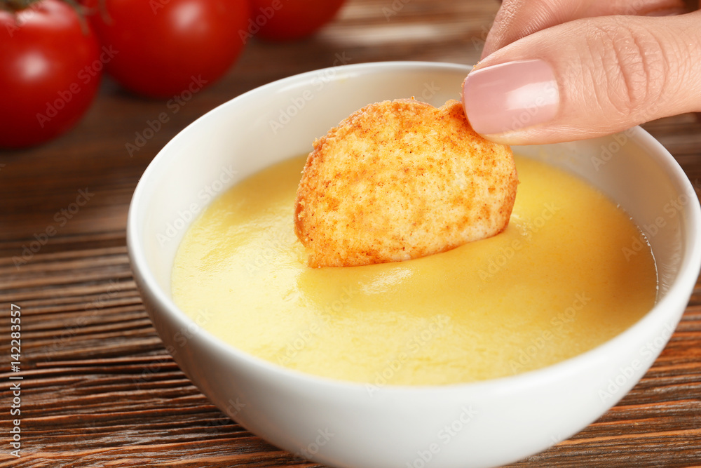Dipping chips into bowl with cheese sauce on dining table Dipping chips into bowl with cheese sauce on dining table