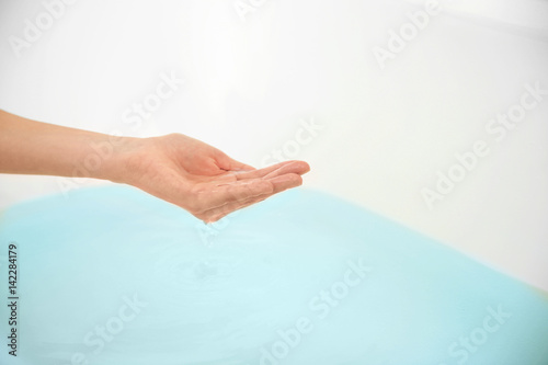 Female hand determining temperature of water in bathtub