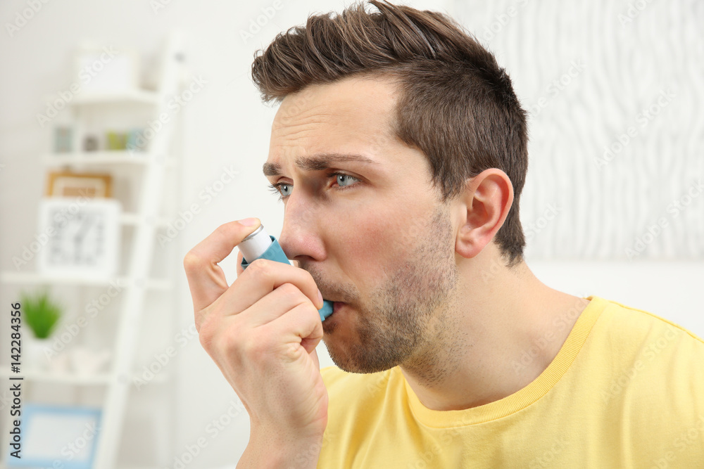 Young man using inhaler during asthmatic attack at home