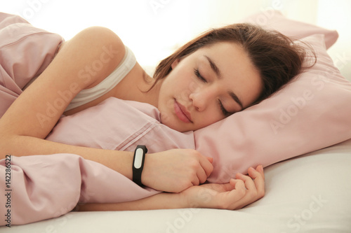 Young woman with sleep tracker resting in bed at home