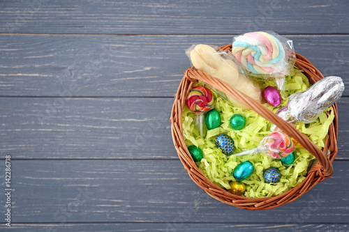 Traditional Easter basket with colorful lollipops and chocolate eggs on wooden background