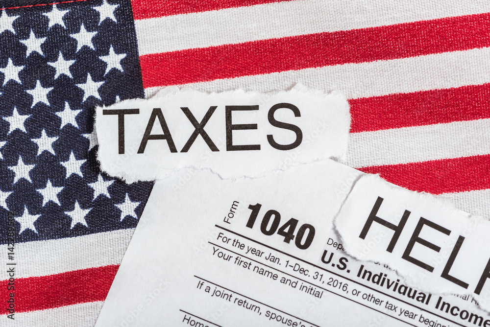Fototapeta premium 1040 tax form with word taxes in torn paper on American Flag and the word help.