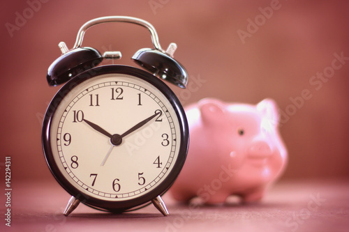 Old fashioned alarm clock with blurred piggy box and vignette