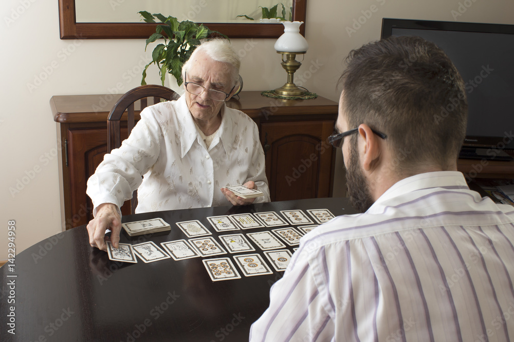 Naklejka premium Wiekowa wróżka stawia karty tarota. Bardzo stara kobieta stawia karty tarota mężczyźnie. Wróżenie z kart tarota.