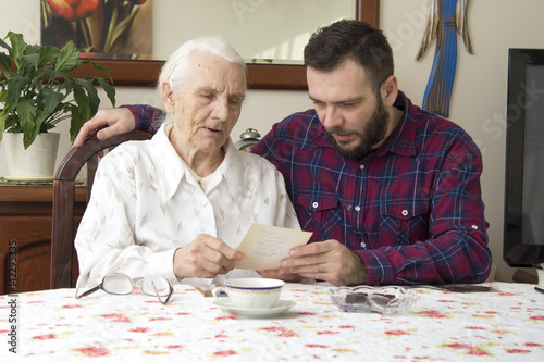 Staruszka z wnuczkiem siedzą przy stole w salonie i oglądają stare zdjęcia.