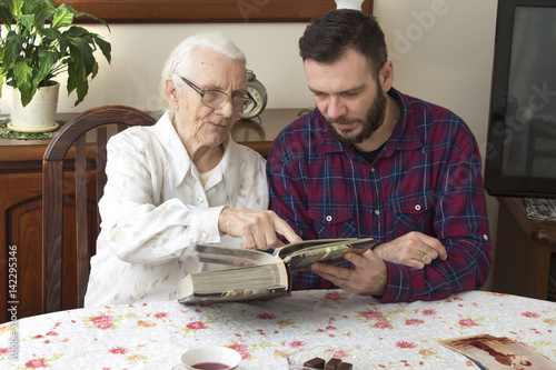 Babcia z wnuczkiem wspominają dawne czasy oglądając album ze zdjęciami.