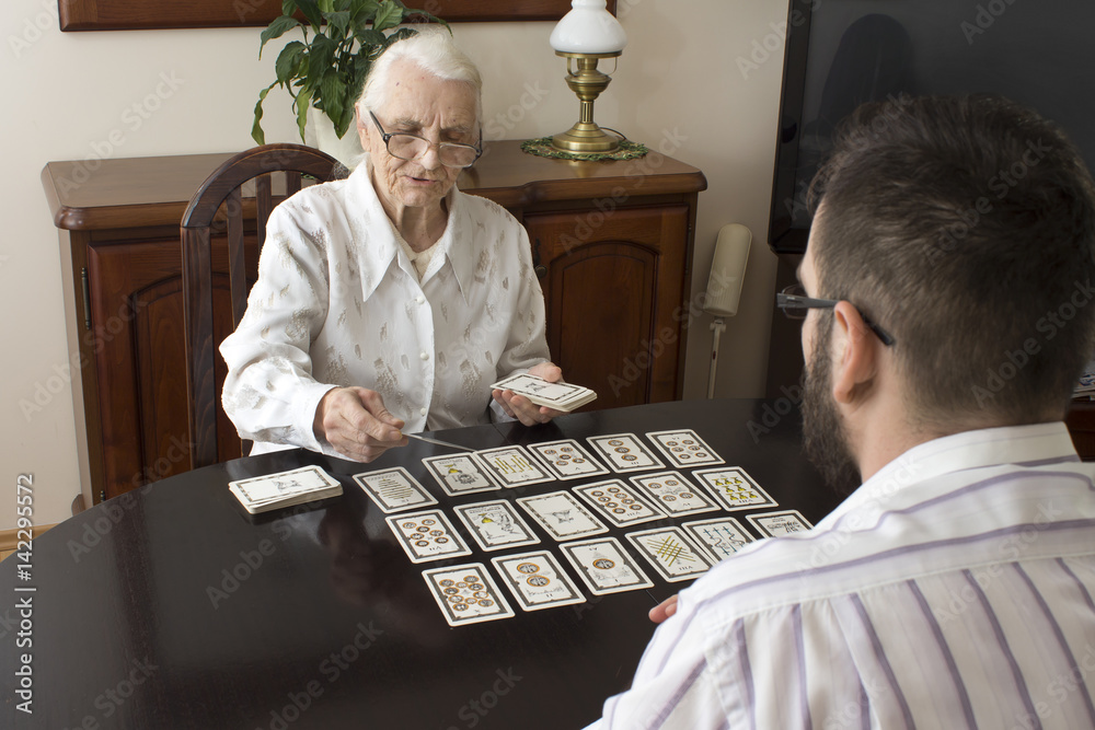 Very old woman puts a man tarot cards. Fortune-telling with tarot cards.