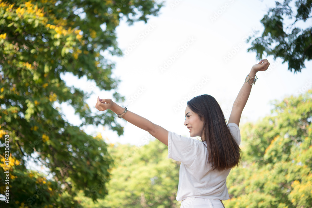 Portrait of teenage girl raising arms and laughing in the park.
