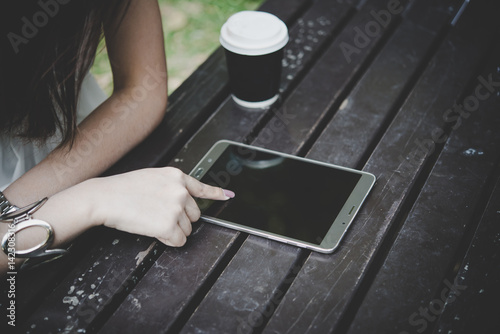 Close up of woman hands holding tablet computer on the wooden table with cup of coffee.