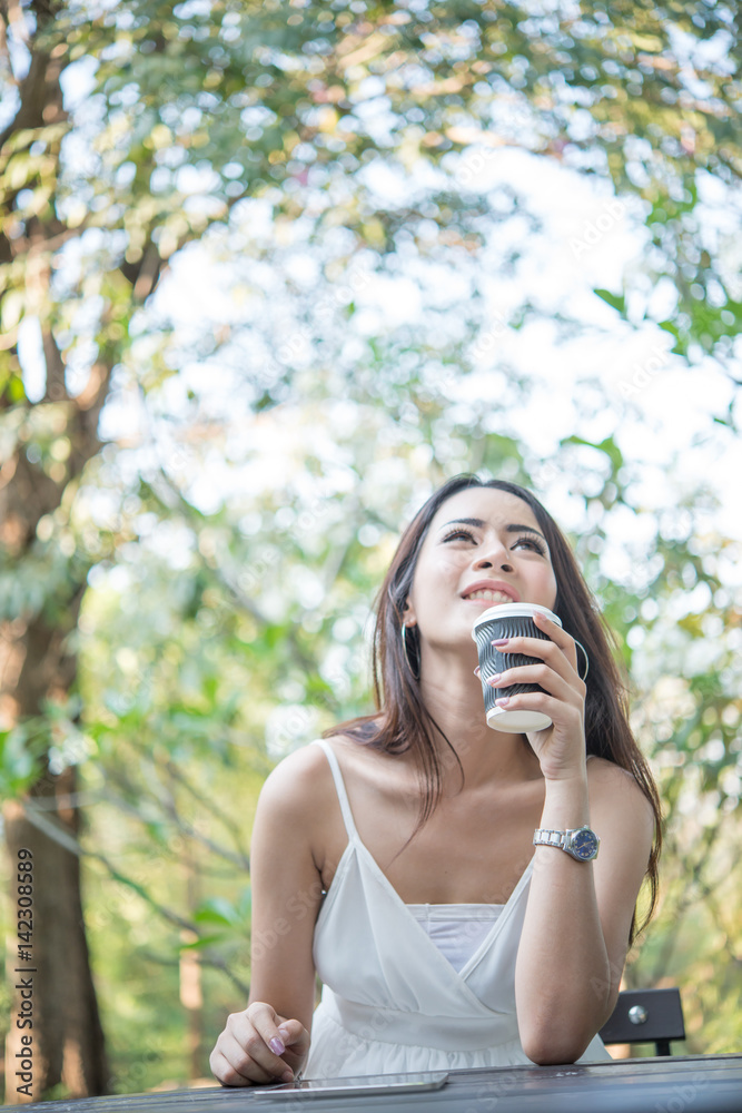 Young woman holding disposable coffee cup while sitting enjoying at nature outdoors. Young woman holding disposable coffee cup while sitting enjoying at nature outdoors.