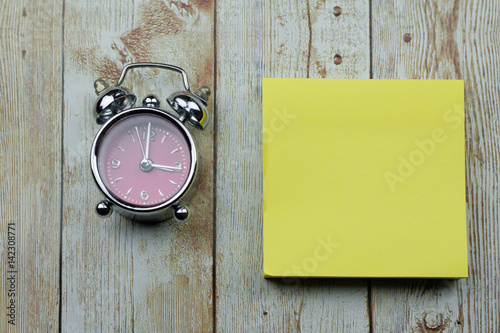 Clock next to blank yellow paper or sticker on wooden background with concept of time and things to do list