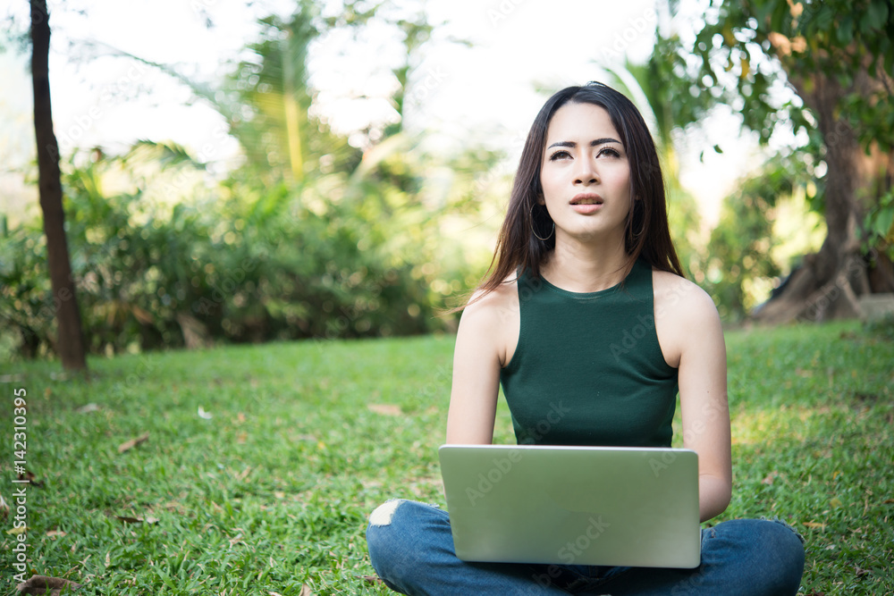 Young beautiful woman sitting on green grass and using laptop in the park with nature background. Young beautiful woman sitting on green grass and using laptop in the park with nature background.
