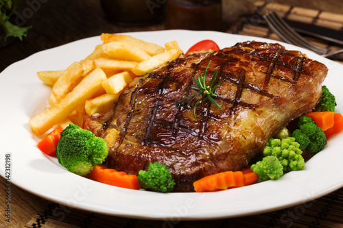 Grilled beef steak served with French fries and vegetables on a white plate.