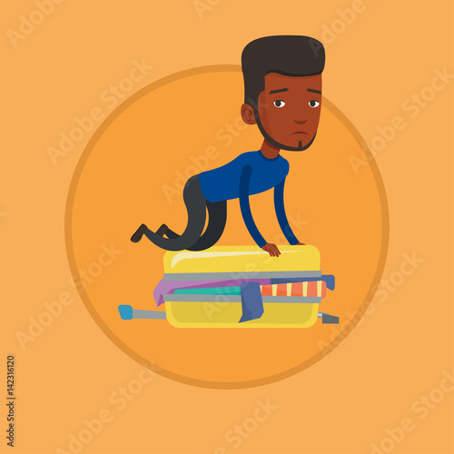 Young man trying to close suitcase.